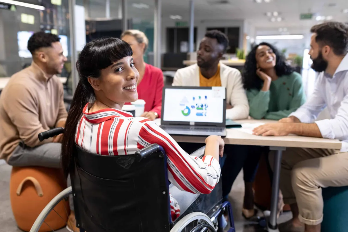 Mulher em cadeira de rodas participa de reunião sobre design acessível, inclusivo e universal com equipe diversa em ambiente corporativo.